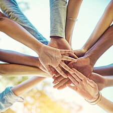 Mehrere junge Menschen stehen im Kreis und legen ihre Hände zur Teamgeste in die Mitte.