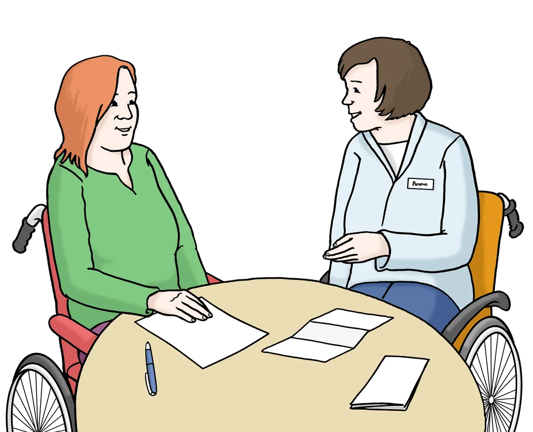 Zwei Frauen sitzen an einem Tisch. Eine Frau sitzt im Rollstuhl. Sie sprechen miteinander und schauen auf Unterlagen.