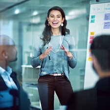 Eine junge Frau präsentiert vor einem Team in einem modernen Büro und erklärt Inhalte an einem Whiteboard mit Haftnotizen.