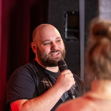 Ein Mann hält ein Mikrofon und spricht bei einer Veranstaltung vor Publikum.