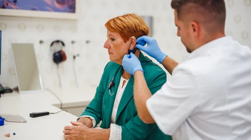 Eine medizinische Fachkraft passt einer Patientin in einer Praxis ein Hörgerät an.