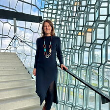 Eine Frau steht auf einer Treppe in einem modernen Glasgebäude und lächelt in die Kamera.