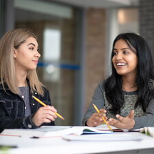 Zwei Studierende sitzen an einem Tisch, diskutieren und arbeiten gemeinsam an Unterlagen.