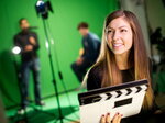Eine Studierende hält eine Filmklappe in einem Medien- oder Filmstudio vor einem Greenscreen.