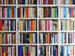 Bunte Bücher stehen eng gedrängt in einem weißen Bücherregal.