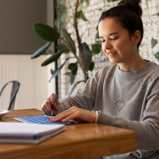 Eine junge Frau sitzt an einem Tisch, arbeitet konzentriert mit Unterlagen und schreibt Notizen in ruhiger Umgebung.